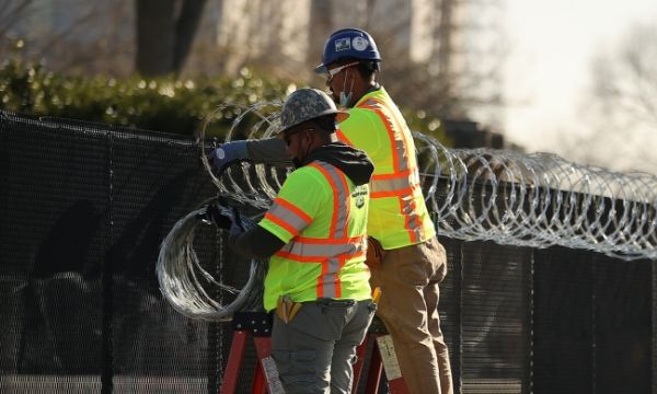 Two workers are installing cross razor wire on the top of the fence.